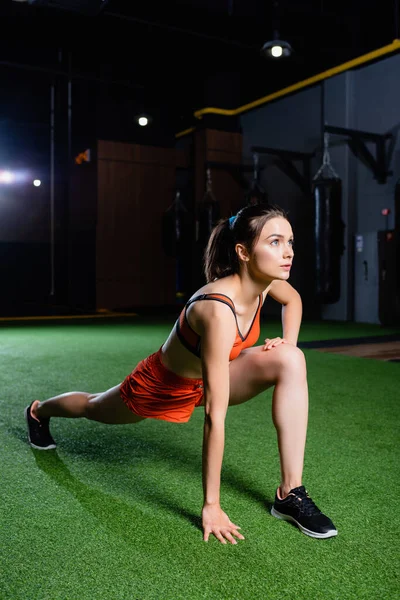Young sportswoman doing forward lunges exercise while warming up in gym — Stock Photo