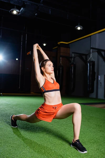 Femme de sport en soutien-gorge et shorts faisant des exercices de fentes avant avec les mains levées — Photo de stock