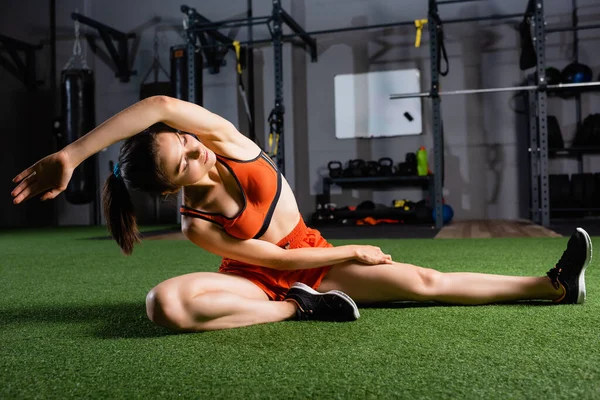 Sportive aux yeux fermés faisant de l'exercice assis de flexion latérale tout en se réchauffant dans la salle de gym — Photo de stock