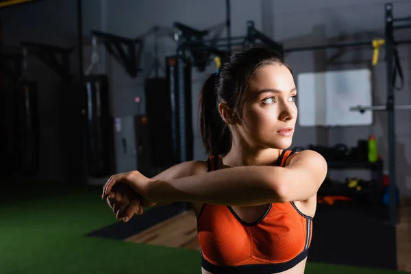 Athletic woman warming up arms and looking away in sports center — Stock Photo