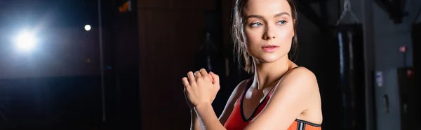 Youngs sportswoman looking away while warming up arms in gym, banner — Stock Photo