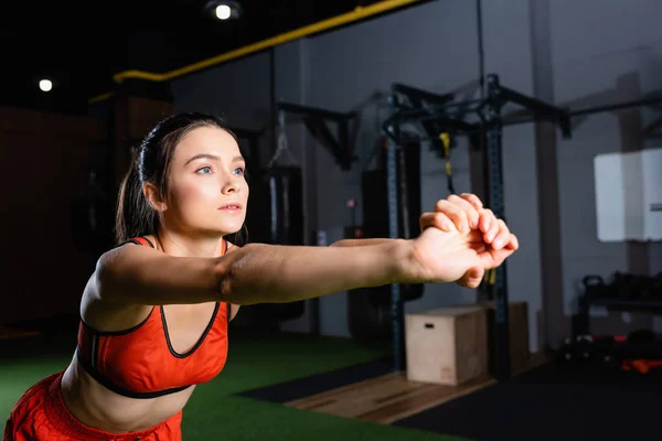 Young sportswoman stretching arms while looking away in gym — Stock Photo