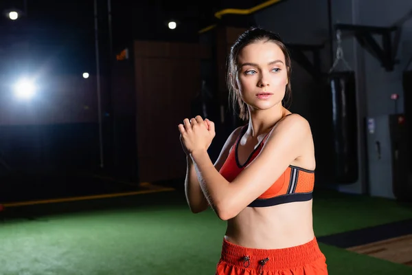 Athletic sportswoman looking away while warming up arms in gym — Stock Photo