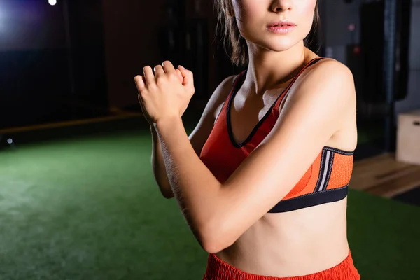 Cropped view of young sportswoman warming up arms while stretching in sports center — Stock Photo