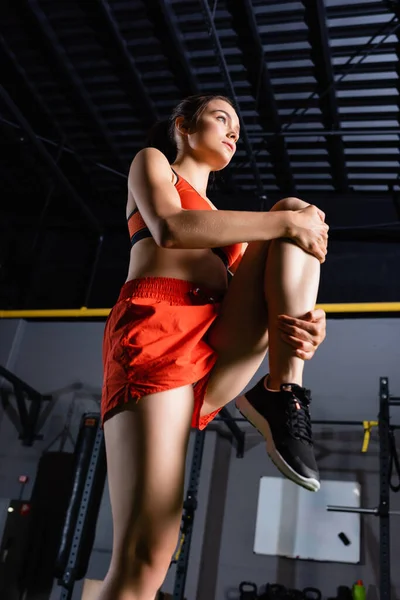Low angle view of sportswoman in shorts stretching leg in sports center — Stock Photo