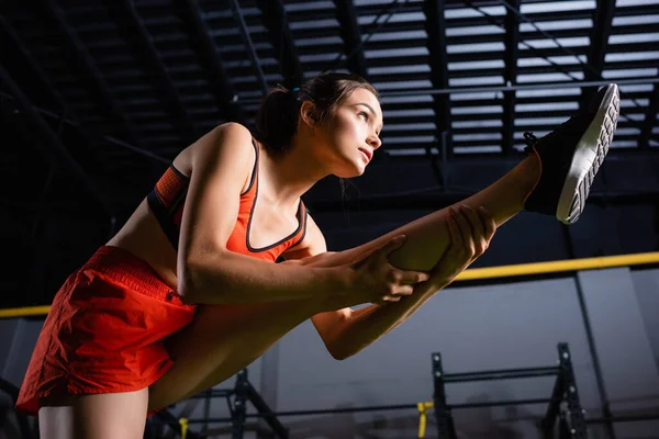 Vista de ángulo bajo de la deportista que estira la pierna mientras entrena en el gimnasio - foto de stock