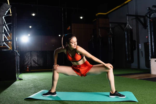 Sportive woman in shorts and top stretching legs while working out in sports center — Stock Photo