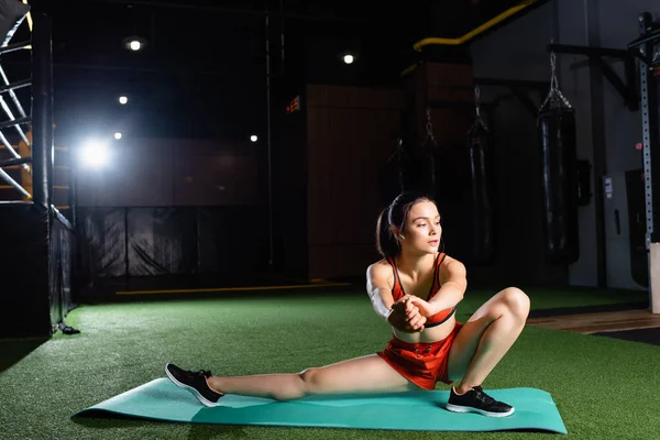 Атлетическая спортсменка растягивает руки и ноги на тренажерном коврике в спортзале — стоковое фото