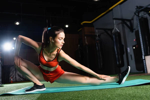 Sportswoman in top and shorts stretching legs on fitness mat in sports center — Stock Photo