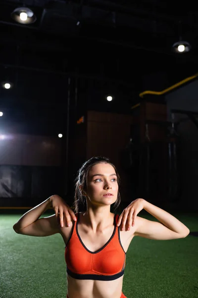 Sportswoman looking away while warming up arms and shoulders in gym — Stock Photo