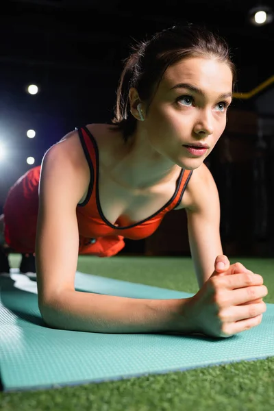 Sportlerin mit Kopfhörer beim Plankentraining im Fitnessstudio — Stockfoto