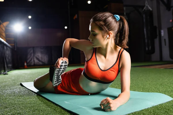 Mulher esportiva em esportes sutiã alongamento perna enquanto deitado no tapete de fitness — Fotografia de Stock