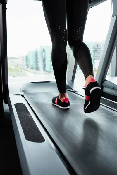 Vista parcial de la deportista en zapatillas de deporte y polainas corriendo en la cinta — Stock Photo