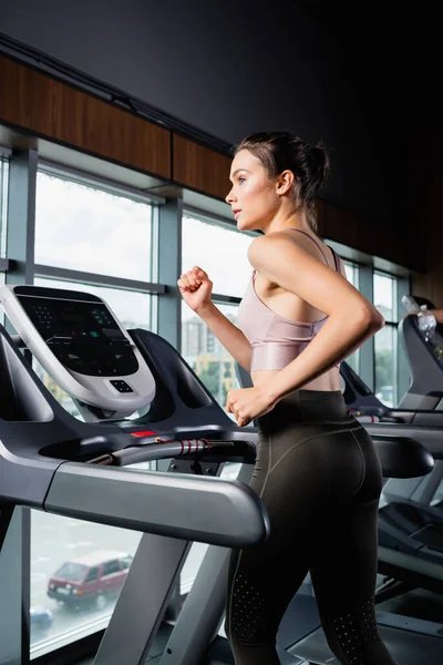 Side view of sportswoman in leggings looking away while running on treadmill — Stock Photo