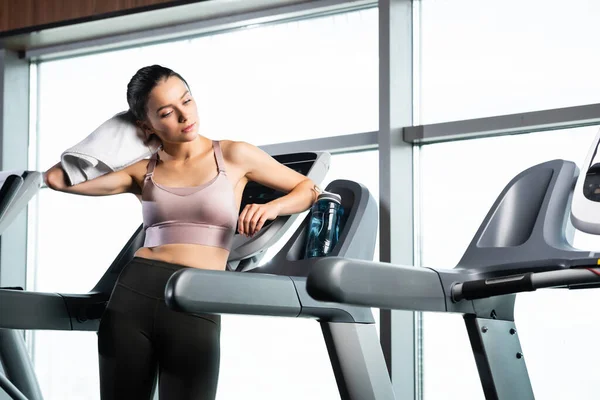 Sportswoman in bra and leggings wiping neck with towel while standing on treadmill — Stock Photo