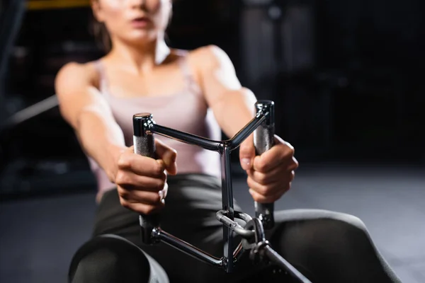 Partial view of sportswoman training on rowing machine in sports center on blurred background — Stock Photo