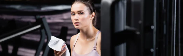 Young sportswoman looking at camera while holding towel in gym, banner — Stock Photo