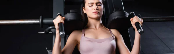 Vista superior de la deportista con los ojos cerrados entrenamiento en la máquina de ejercicios de extensión de brazos, bandera - foto de stock