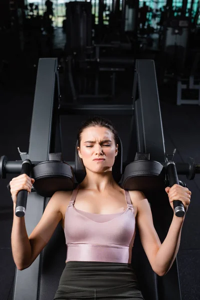 Vista superior de la deportista con los ojos cerrados entrenamiento en la máquina de extensión de brazos en el gimnasio - foto de stock