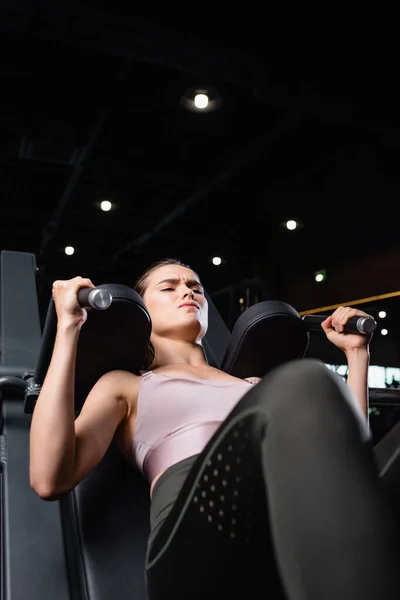 Athletic sportswoman doing arms extension exercise on training machine on blurred foreground — Stock Photo