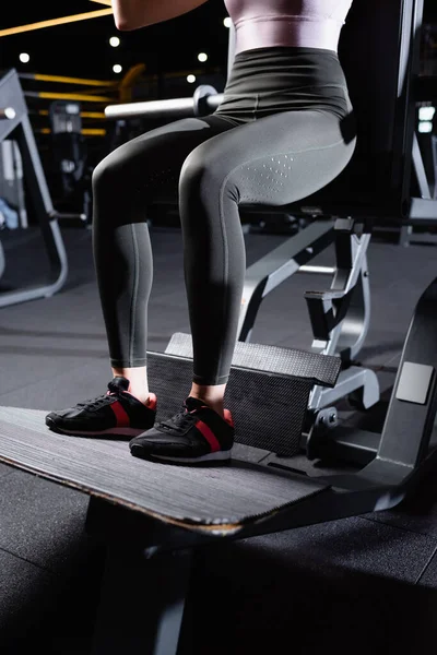 Partial view of sportswoman in leggings and sneakers training on exercising machine — Stock Photo
