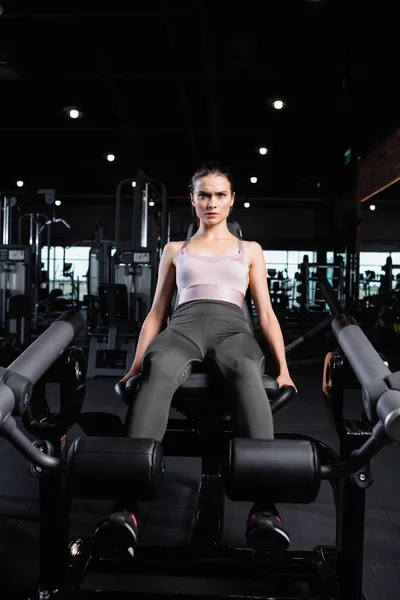 Sportswoman in top and leggings excersining on leg extension machine — Stock Photo