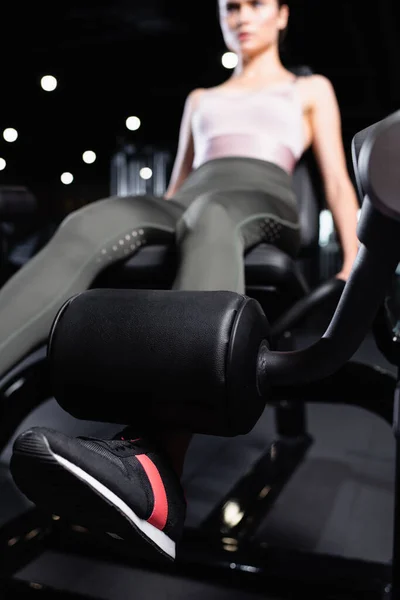 Молода спортсменка робить вправи для розширення ніг на тренувальній машині на розмитому фоні — стокове фото