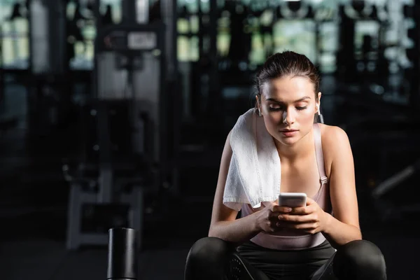 Messaggistica sportiva sul cellulare mentre sei seduto in palestra con asciugamano sulla spalla — Foto stock