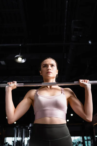 Young sportswoman in bra lifting power rack in gym — Stock Photo
