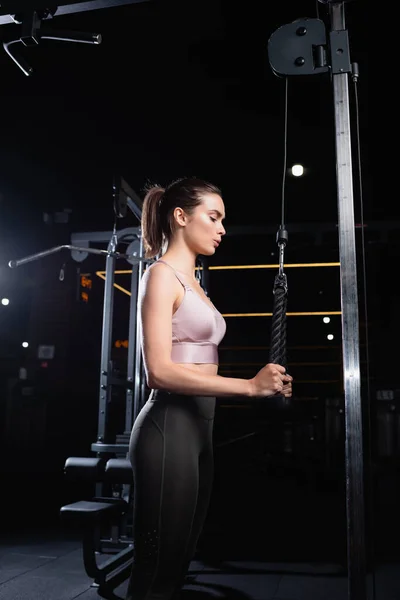 Vista lateral da esportista em cima e leggings trabalhando na máquina de extensão triceps — Fotografia de Stock