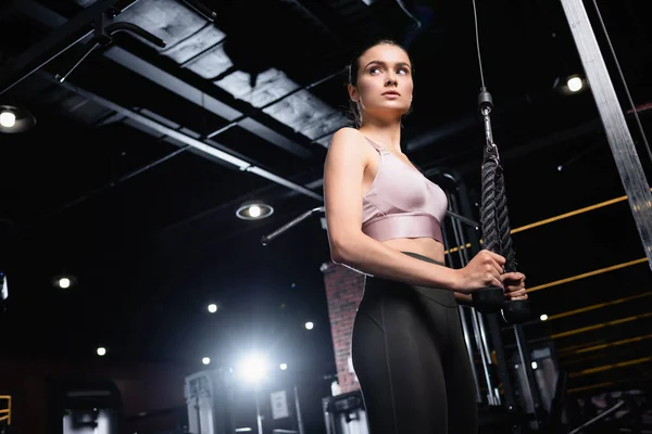 Low angle view of sportswoman looking away while training on cable pushdown machine — Stock Photo