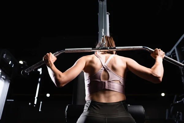 Vista posteriore della donna sportiva che fa esercizio di braccia e schiena estensione sulla macchina lat — Foto stock