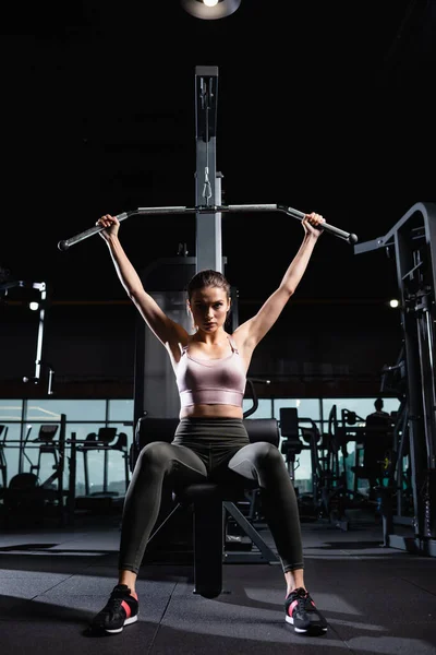 Joven deportista mirando a la cámara mientras entrena en la máquina lat en el gimnasio — Stock Photo