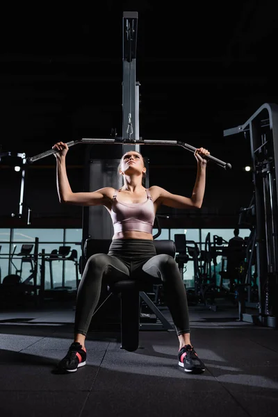 Sportswoman in top and leggings working out on lat machine in sports center — Stock Photo