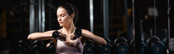 Joven deportista sentado y haciendo ejercicio con pesas en el gimnasio, pancarta - foto de stock