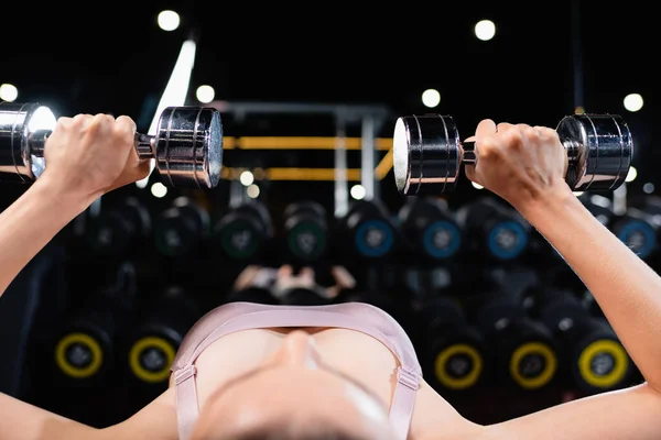 Sportswoman exercising with dumbbells in lying position on blurred foreground — Stock Photo