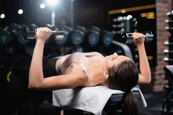 Sportive woman training with dumbbells in lying position in sports center — Stock Photo