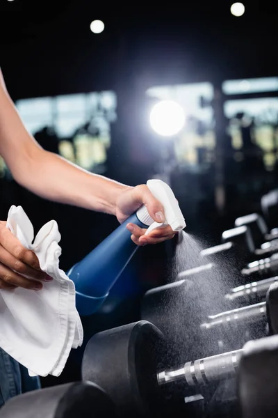 Vista ritagliata di charwoman spruzzando detergente durante la pulizia dei manubri in palestra — Foto stock