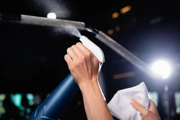 Partial view of charwoman spraying detergent on sports equipment in gym — Stock Photo