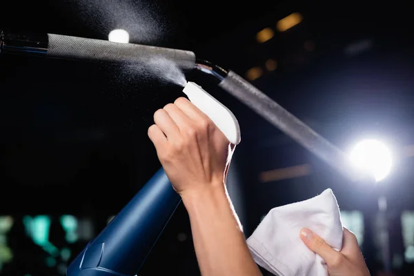 Vue partielle du détergent de pulvérisation de charwoman sur l'équipement sportif dans la salle de gym — Photo de stock