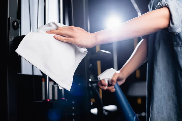 Vue recadrée de charwoman essuyant la machine d'exercice dans la salle de gym sur fond flou — Photo de stock