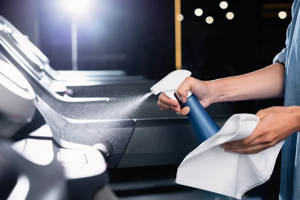 Partial view of charwoman holding rag while spraying cleanser on treadmill in gym on blurred foreground — Stock Photo