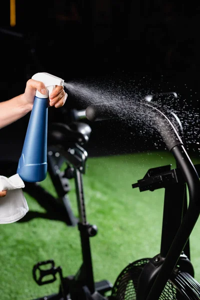 Partial view of charwoman spraying cleanser on sports equipment in gym — Stock Photo