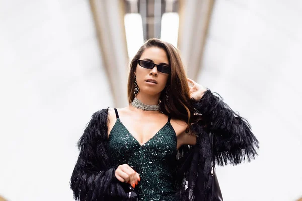 Stylish woman in black lurex dress and sunglasses holding wine bottle at underground station — Stock Photo