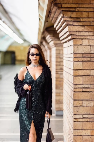 Elegante Frau im schwarzen Lurexkleid steht mit Weinflasche und Handtasche auf U-Bahn-Station — Stockfoto