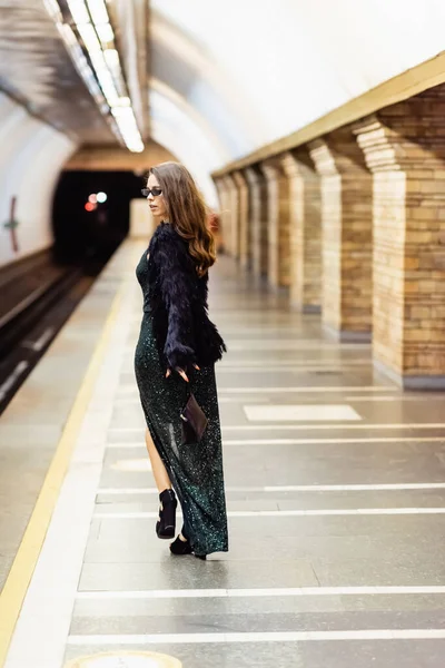 Élégante femme en robe de lurex noir et lunettes de soleil marchant le long de la plate-forme de métro — Photo de stock