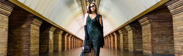 Fashionable woman in long black dress and sunglasses posing at underground station, banner - foto de stock