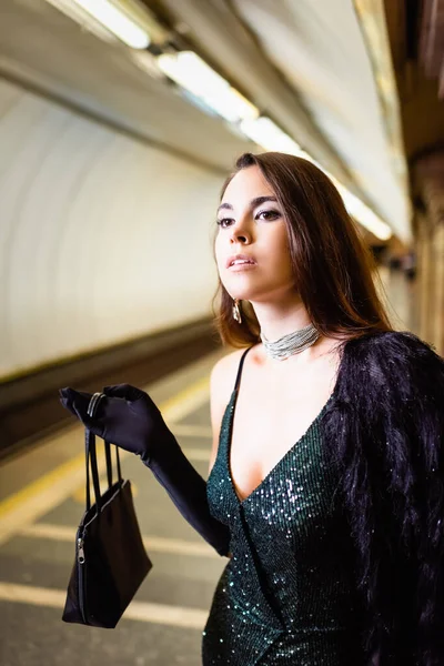 Елегантна молода жінка, дивлячись далеко, стоячи на платформі метро з сумкою — стокове фото