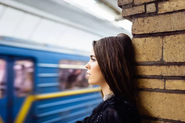 Young woman looking at blurred train while standing on platform near brick column — Stock Photo