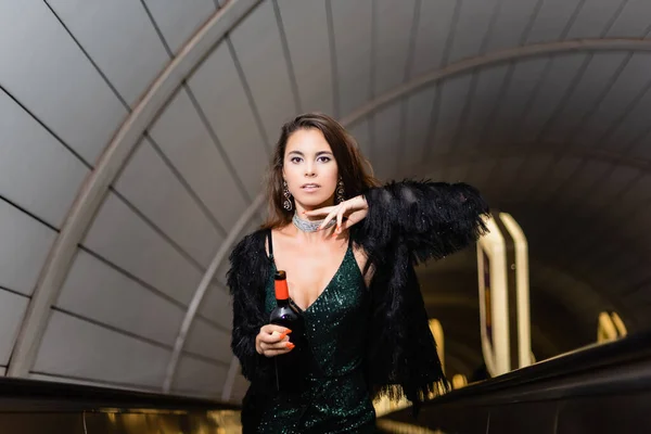 Vue recadrée de glamour femme posant sur escalator avec bouteille de vin — Photo de stock